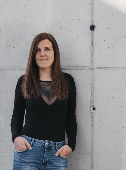 Stefanie Zrim als COO und HR-Verantwortliche in professioneller Pose vor einer Sichtbetonwand.